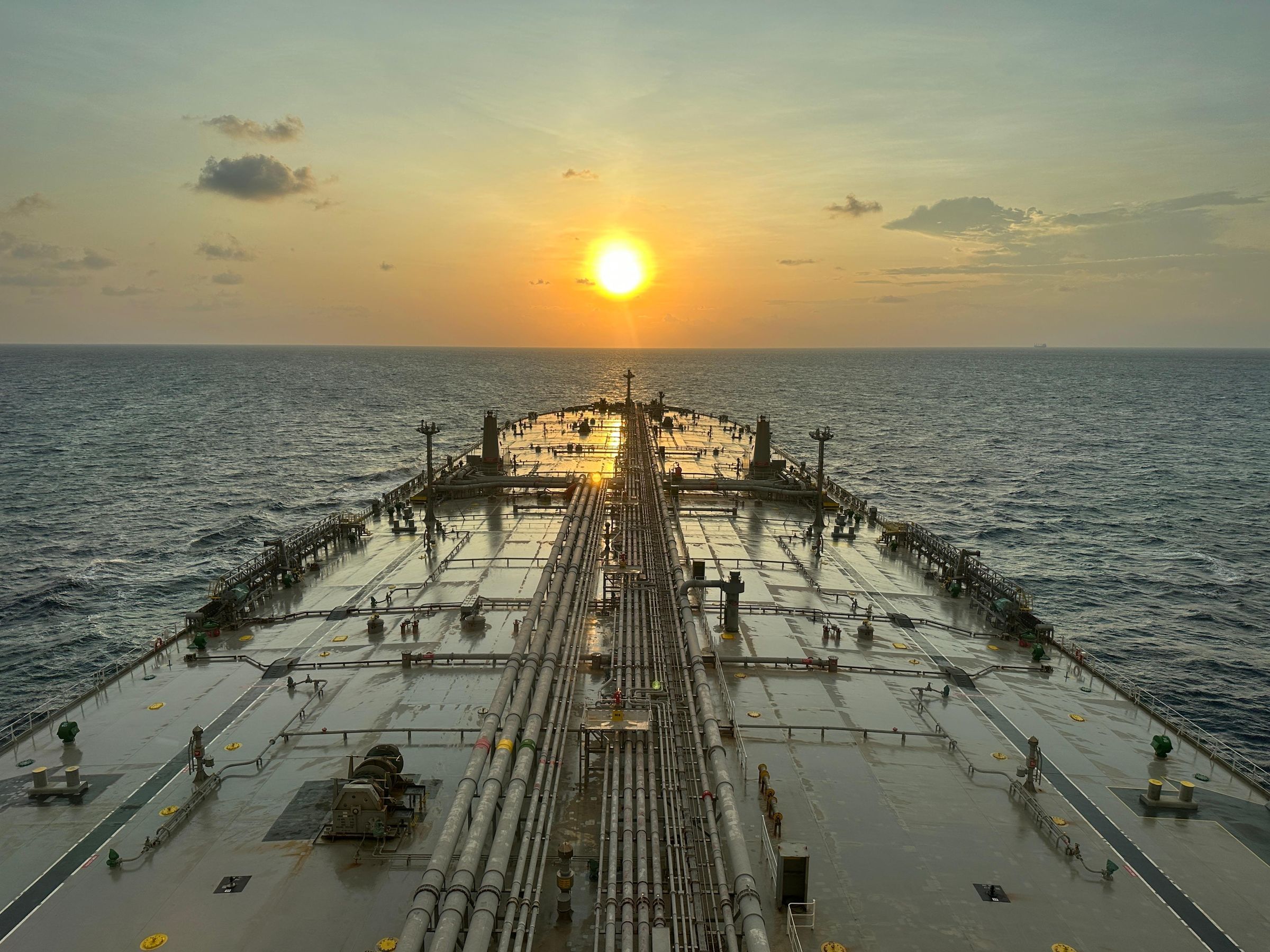 The deck of a tanker at sea, looking towards the sunset on the horizon